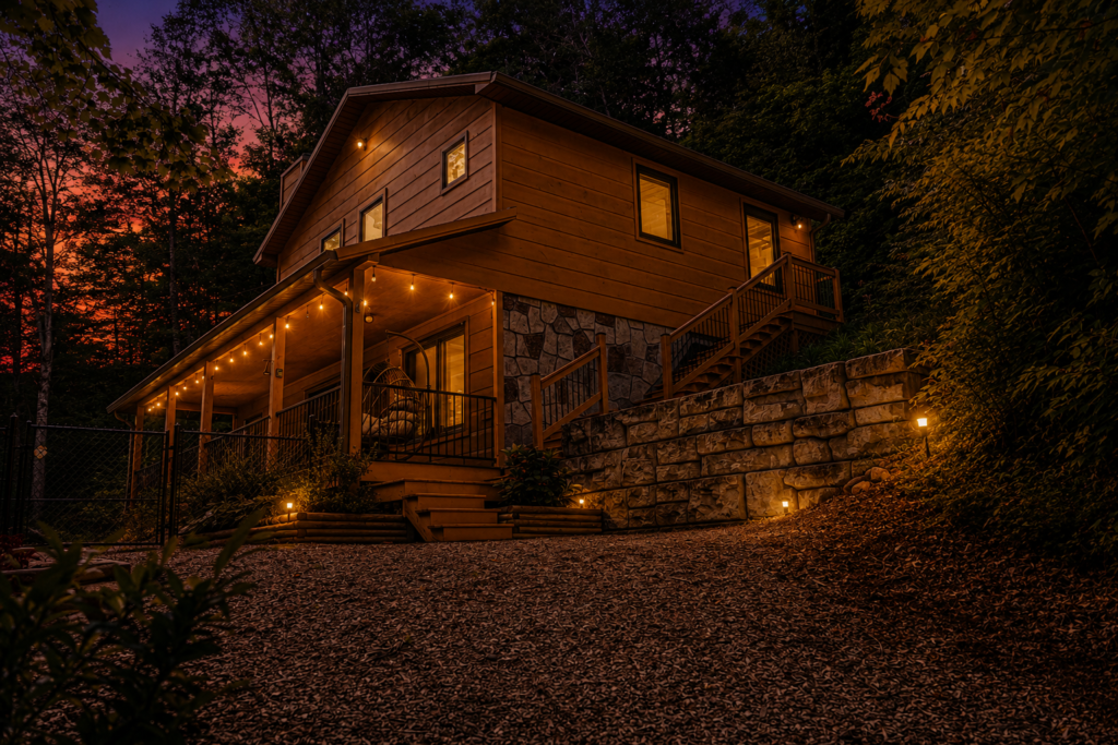 After the Trail cabin illuminated at dusk with warm porch lights and peaceful wooded surroundings.