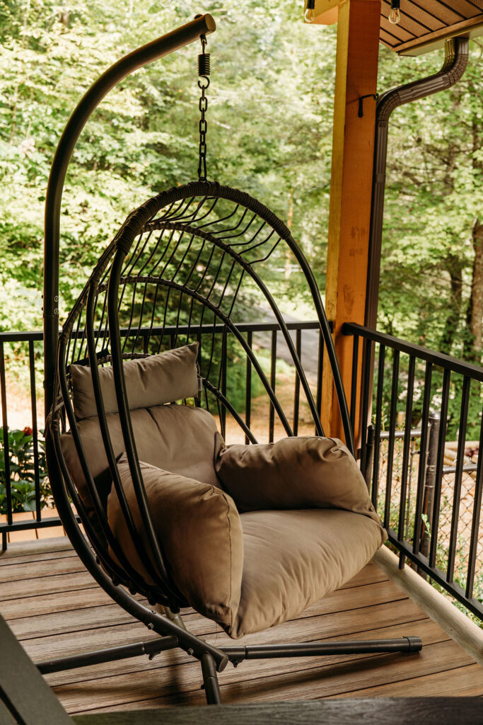 Cozy hanging egg chair with cushions on the covered porch of After the Trail cabin.