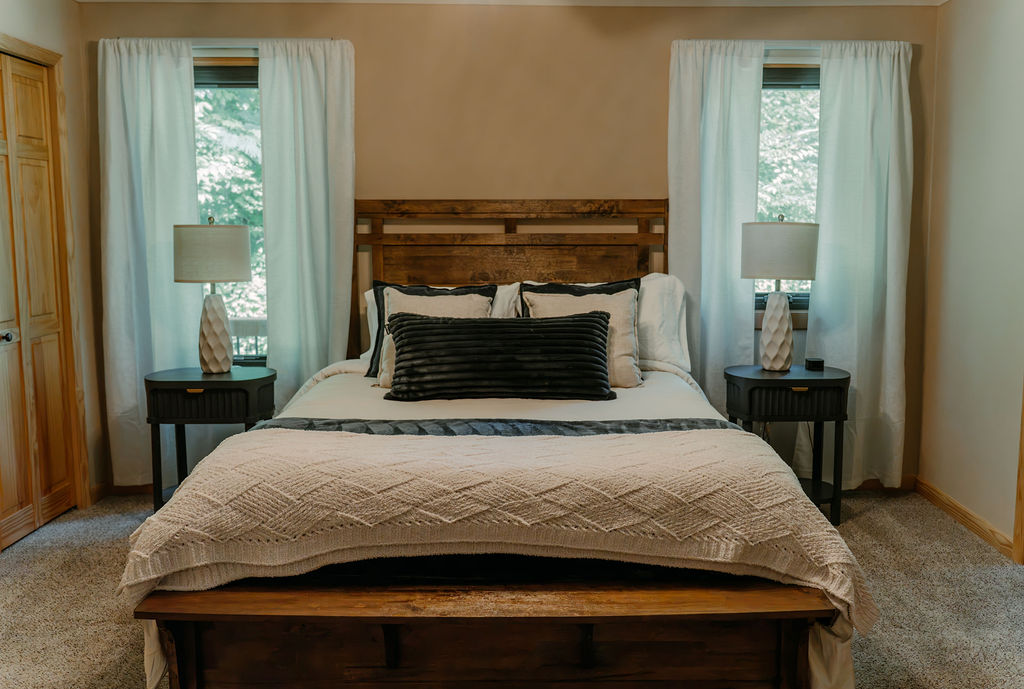 Comfortable queen bed with wooden headboard and natural light from two bedroom windows.