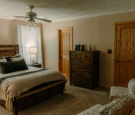 Cozy queen bedroom with wooden headboard, ceiling fan, and rustic furnishings at After the Trail.